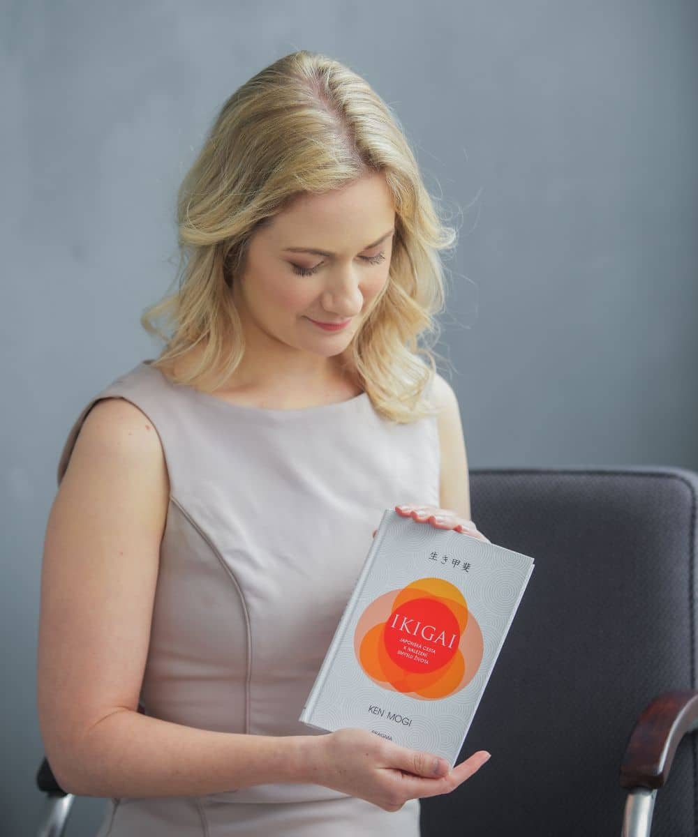Najdi svůj směr - Ikigai koučink pro podnikatelky Kateřina Machek sedí na židli s knihou Ikigai v ruce a zve ženy na online kurz Objev své Ikigai